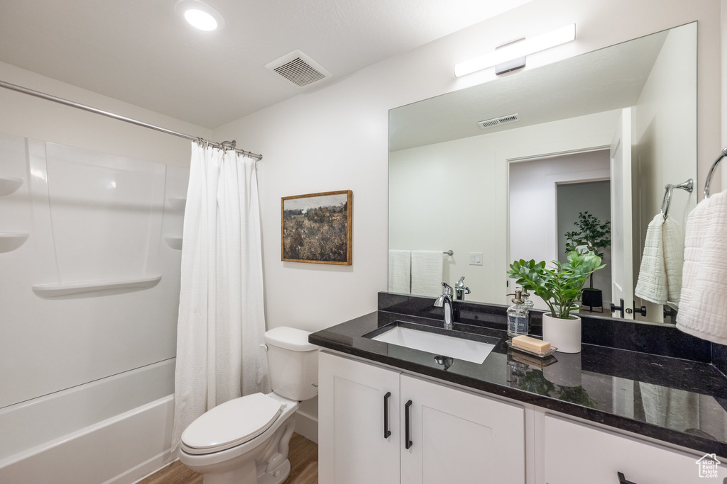 Bathroom with wood finished floors, vanity, and shower / bath combo with shower curtain