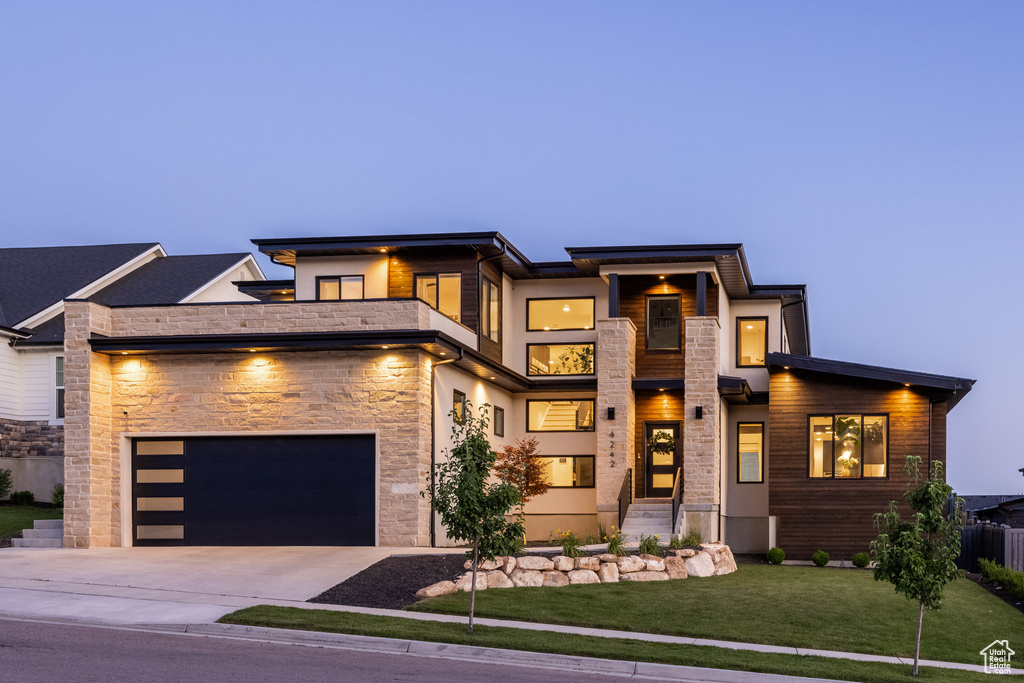 View of front facade with concrete driveway, stone siding, a garage, and a balcony