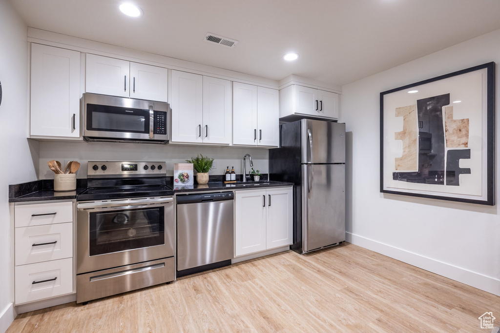 Kitchen with stainless steel appliances, light wood-style flooring, white cabinetry, and recessed lighting