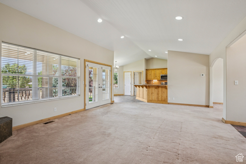 Unfurnished living room featuring vaulted ceiling, light colored carpet, arched walkways, recessed lighting, and french doors