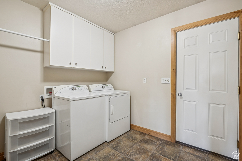Washroom with cabinet space, dark stone finish flooring, washing machine and clothes dryer, and a textured ceiling