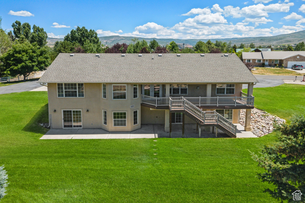 Rear view of property featuring a patio, a deck with mountain view, stucco siding, stairs, and a lawn