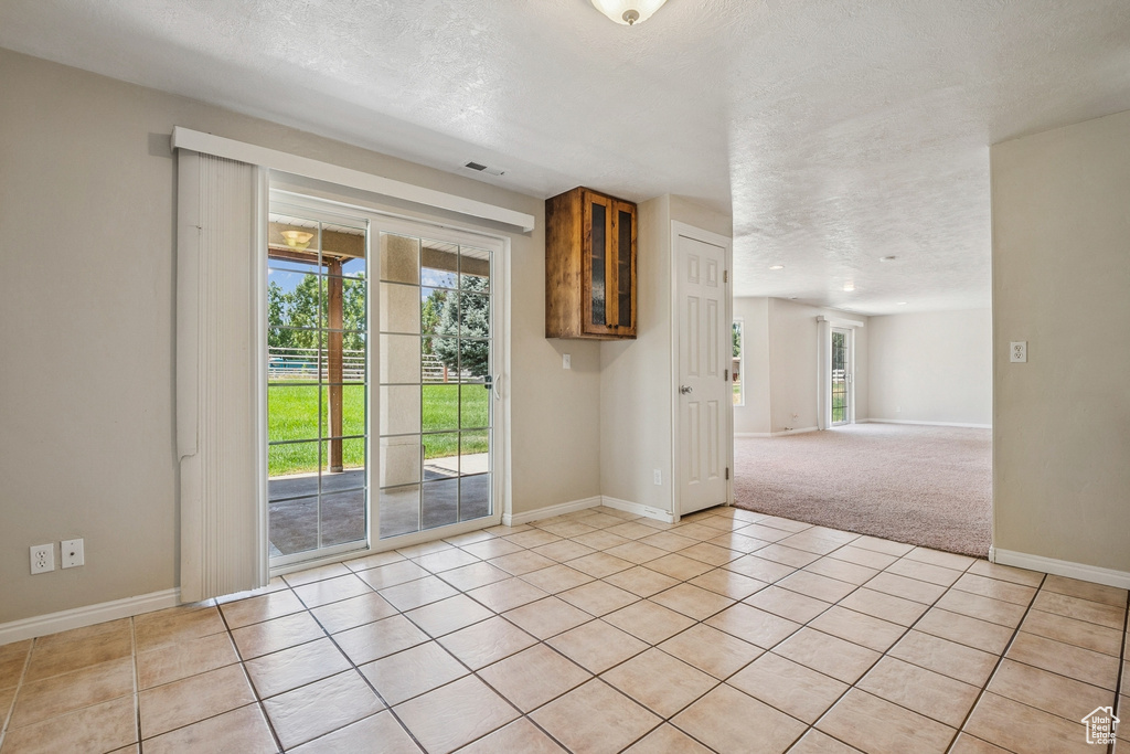 Spare room with a textured ceiling, light tile patterned floors, and light carpet