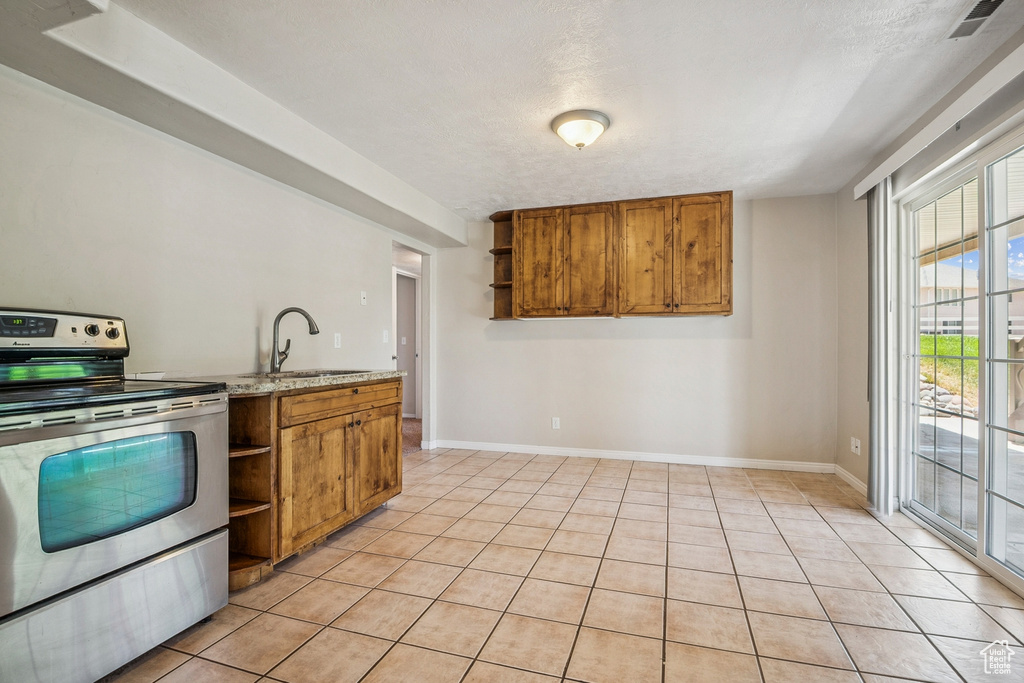 Kitchen with stainless steel range with electric cooktop, open shelves, brown cabinets, light tile patterned flooring, and light stone countertops