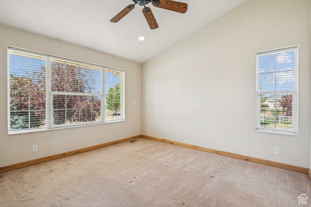 Carpeted empty room with lofted ceiling and a ceiling fan