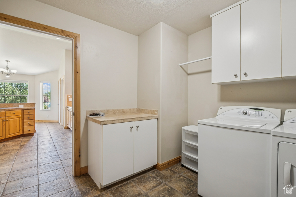 Laundry area with washing machine and dryer, cabinet space, a chandelier, and stone tile flooring