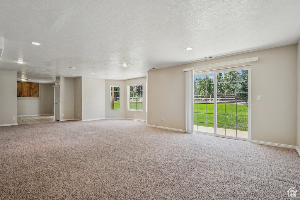 Unfurnished living room with plenty of natural light, carpet, a textured ceiling, and recessed lighting