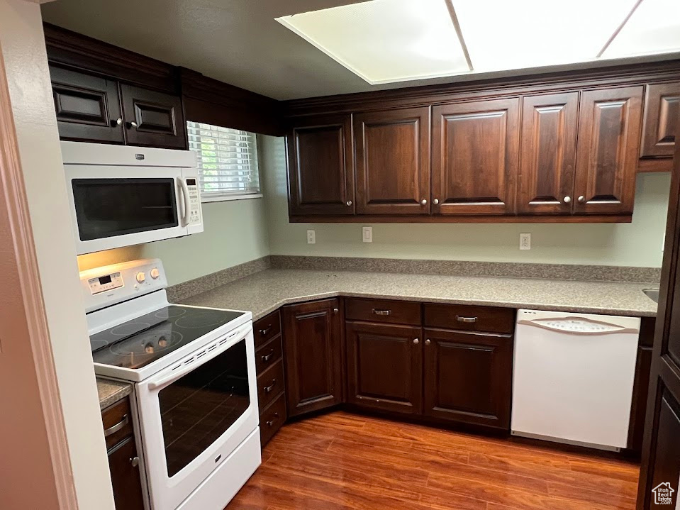 Kitchen with white appliances, dark brown cabinetry, wood finished floors, and light countertops