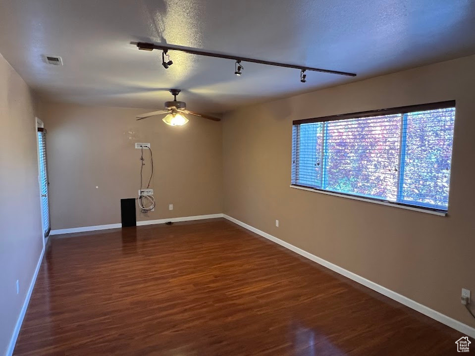 Empty room featuring rail lighting, ceiling fan, and dark wood-type flooring