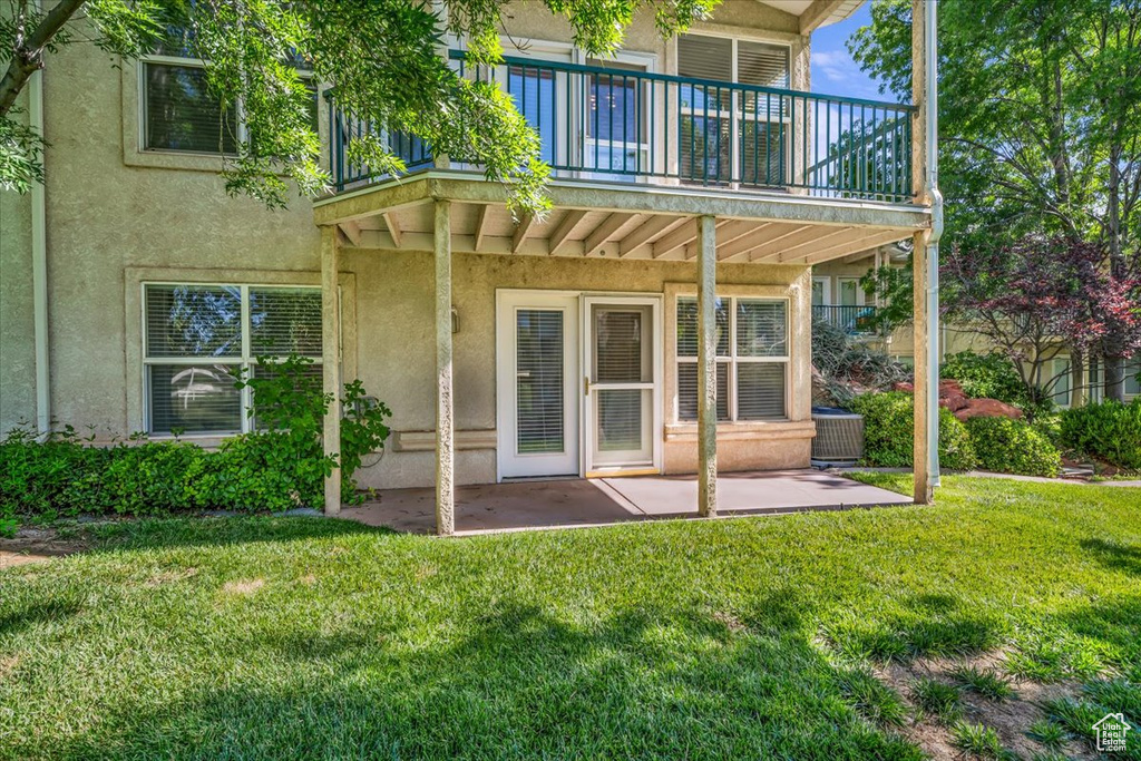 Back of house featuring stucco siding, a patio, a lawn, and a balcony