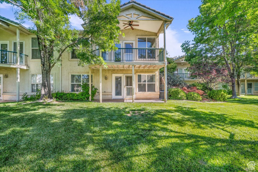 Rear view of property featuring stucco siding, a yard, a ceiling fan, and a balcony