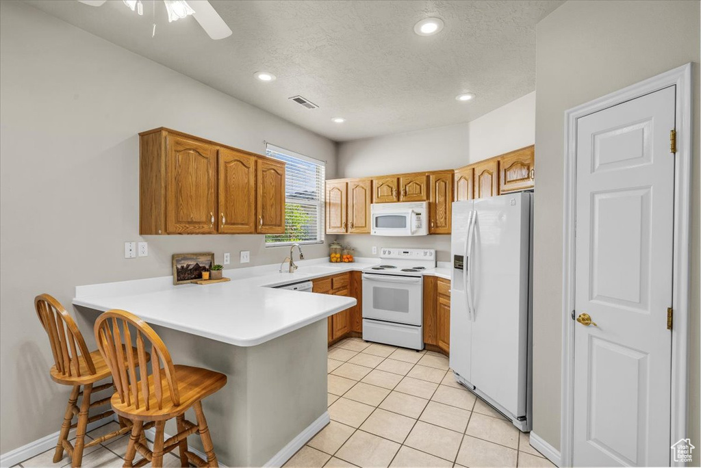 Kitchen with white appliances, a peninsula, a textured ceiling, brown cabinets, and a kitchen breakfast bar
