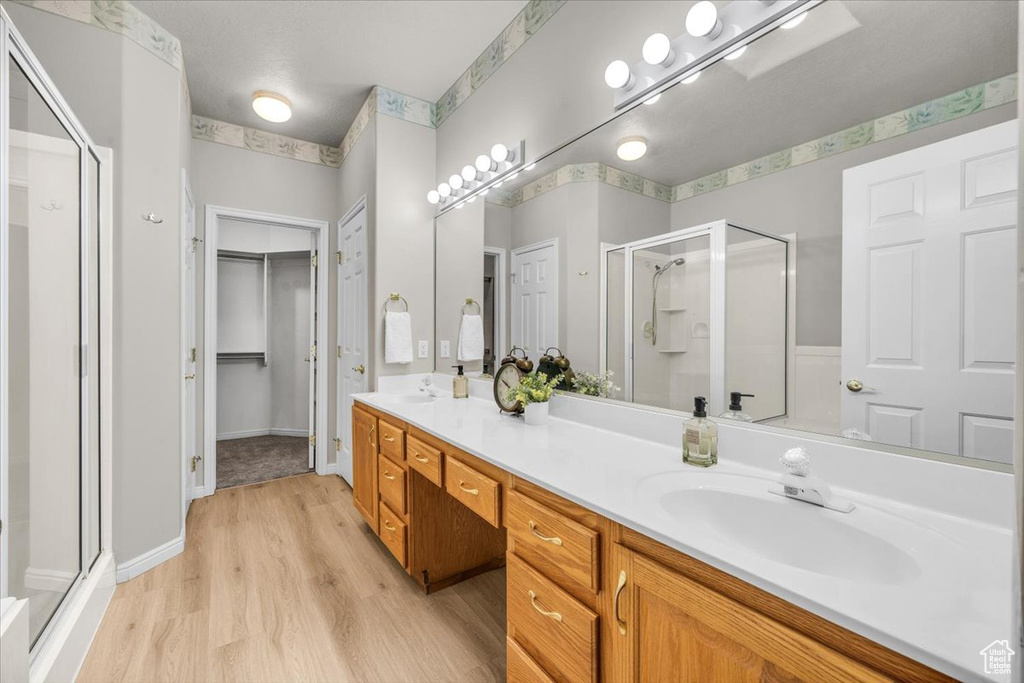 Bathroom featuring a shower stall, wood finished floors, double vanity, and a spacious closet