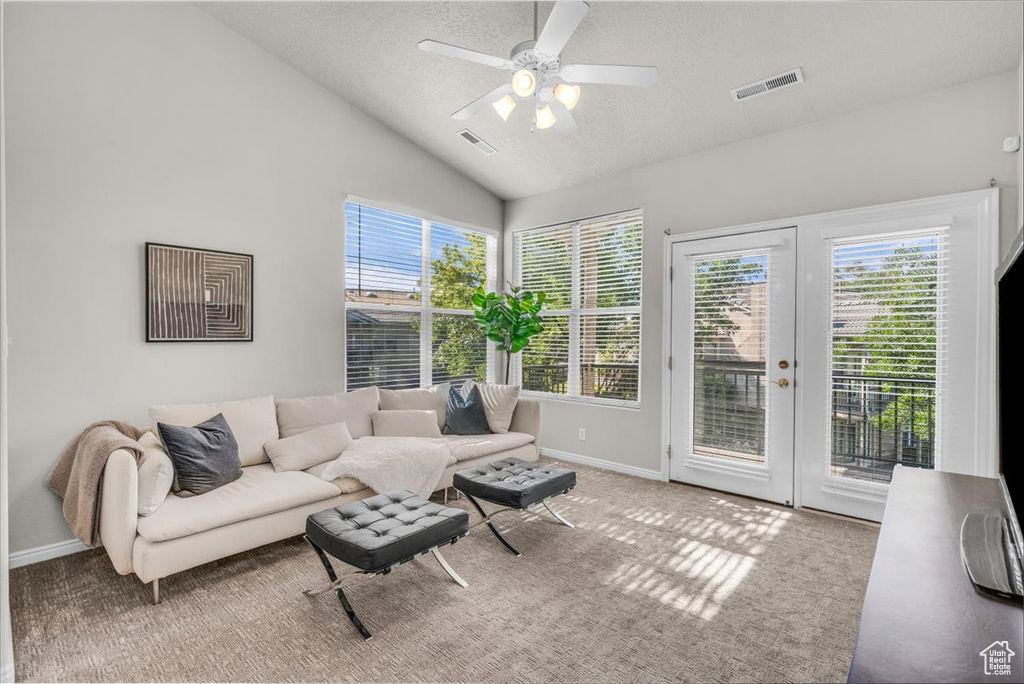 Carpeted living area with vaulted ceiling, plenty of natural light, a ceiling fan, and a textured ceiling