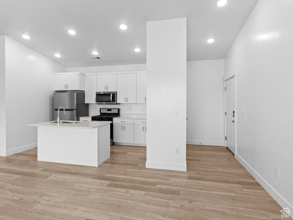 Kitchen featuring appliances with stainless steel finishes, white cabinets, recessed lighting, an island with sink, and light countertops