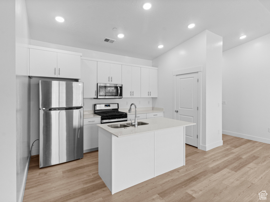 Kitchen featuring stainless steel appliances, a center island with sink, white cabinets, light countertops, and recessed lighting
