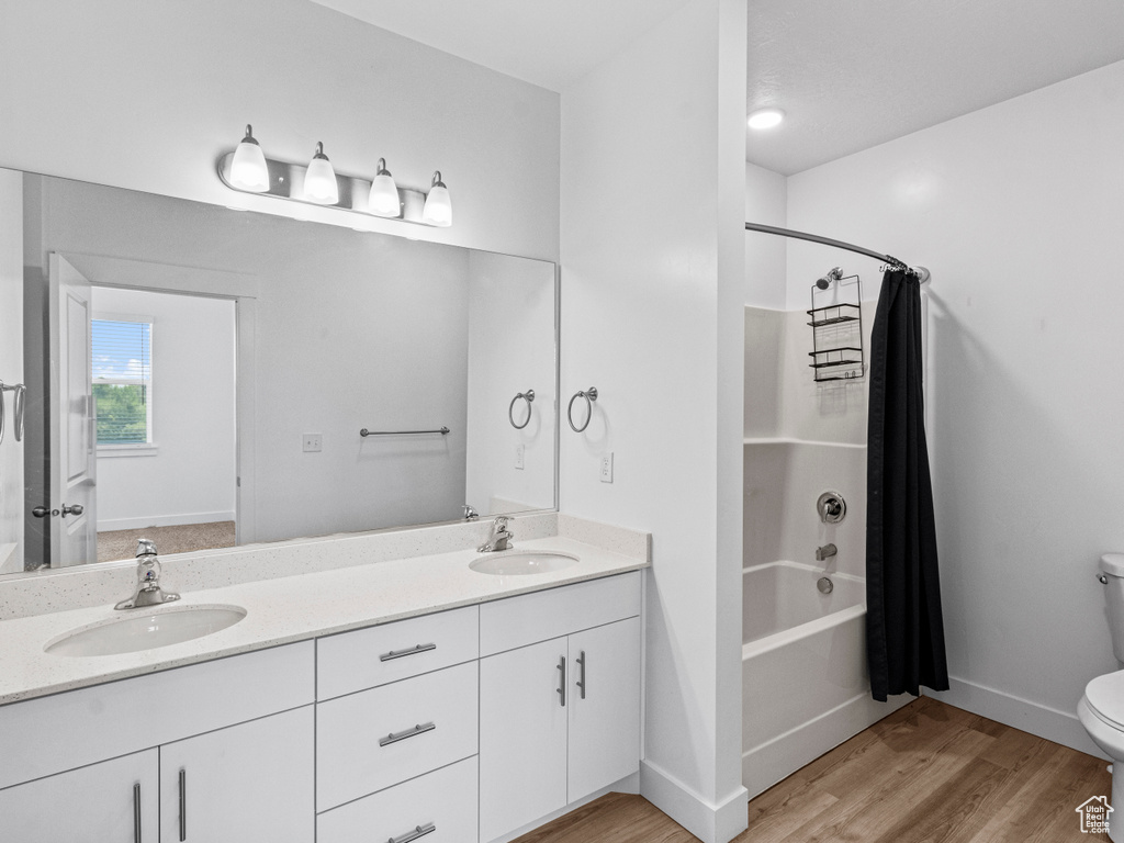 Full bathroom with double vanity, shower / tub combo, and wood finished floors