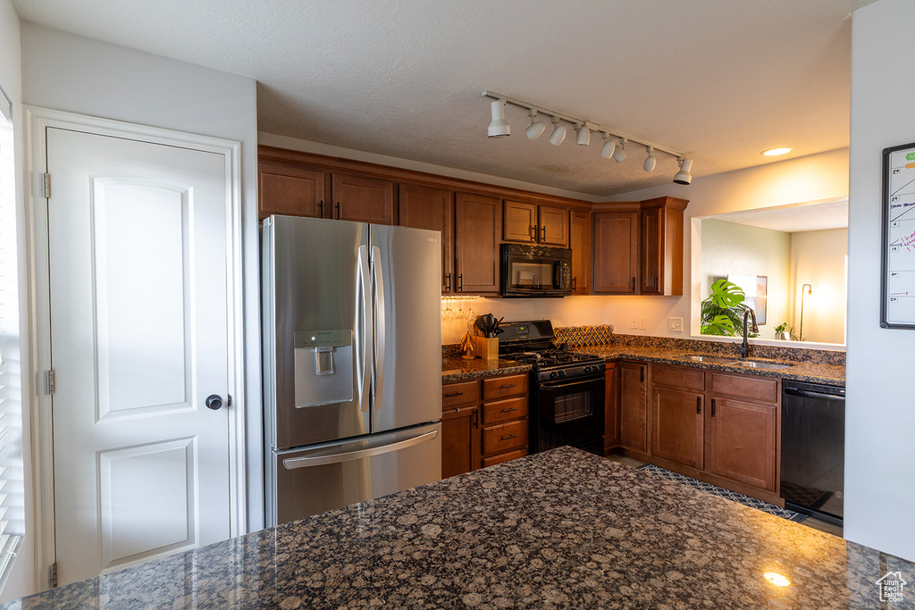 Kitchen featuring black appliances, brown cabinetry, and dark stone countertops