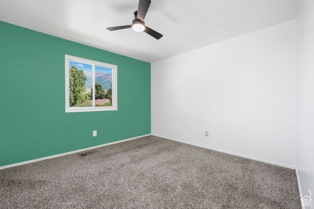 Carpeted empty room featuring a ceiling fan and baseboards