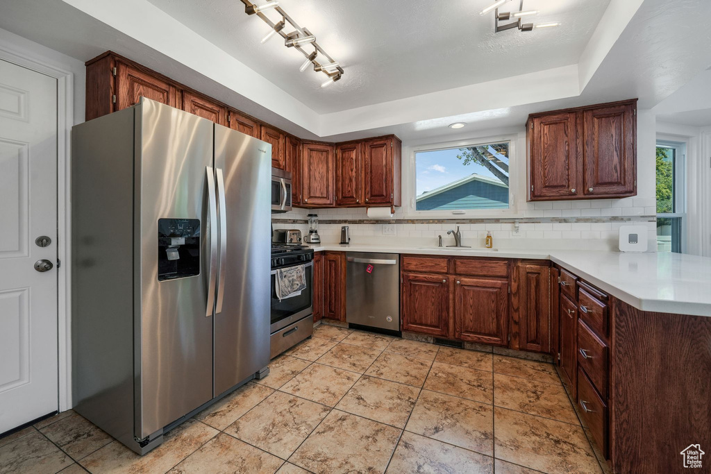 Kitchen featuring stainless steel appliances, decorative backsplash, light countertops, and a peninsula