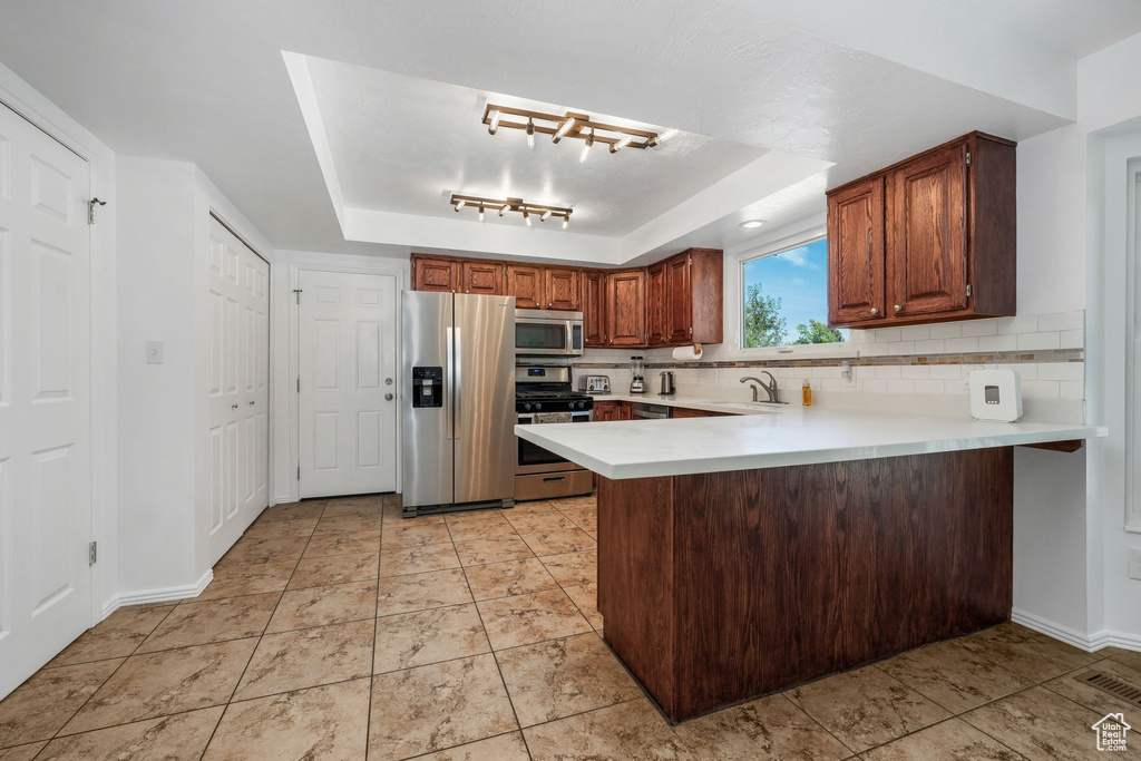 Kitchen with stainless steel appliances, a raised ceiling, light countertops, a peninsula, and tasteful backsplash