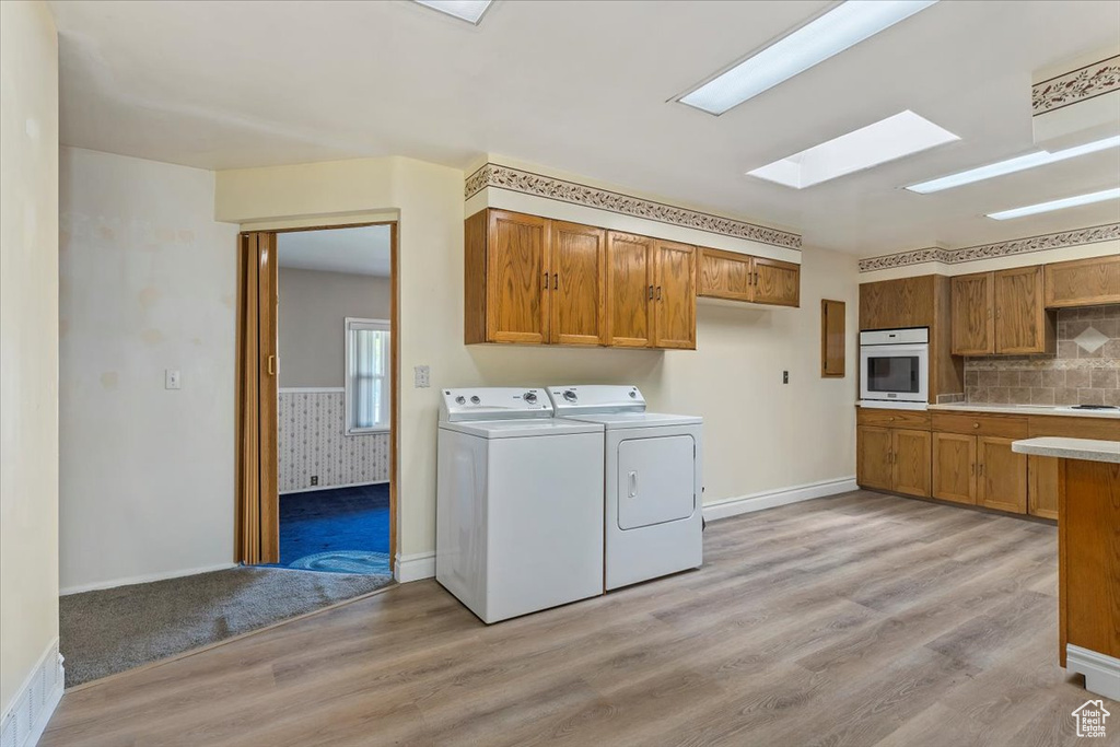Laundry area with a skylight, washer and clothes dryer, and light wood-type flooring