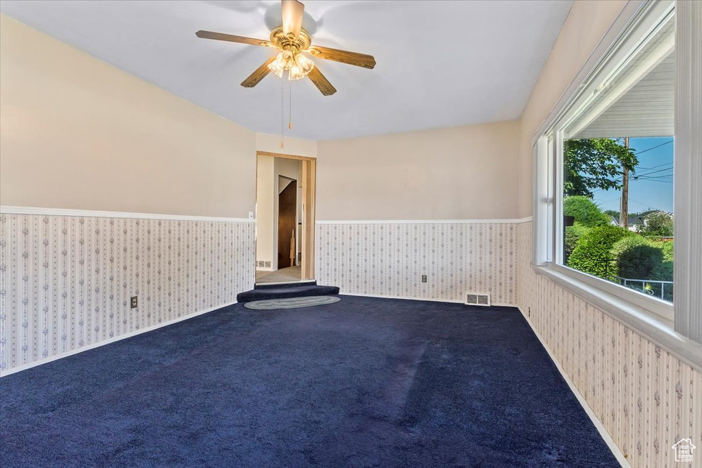 Empty room featuring wallpapered walls, a wainscoted wall, a ceiling fan, and carpet floors