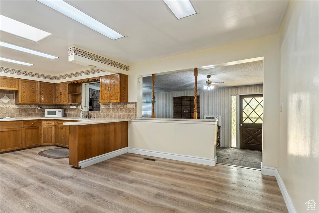 Kitchen featuring white microwave, brown cabinets, open shelves, and backsplash