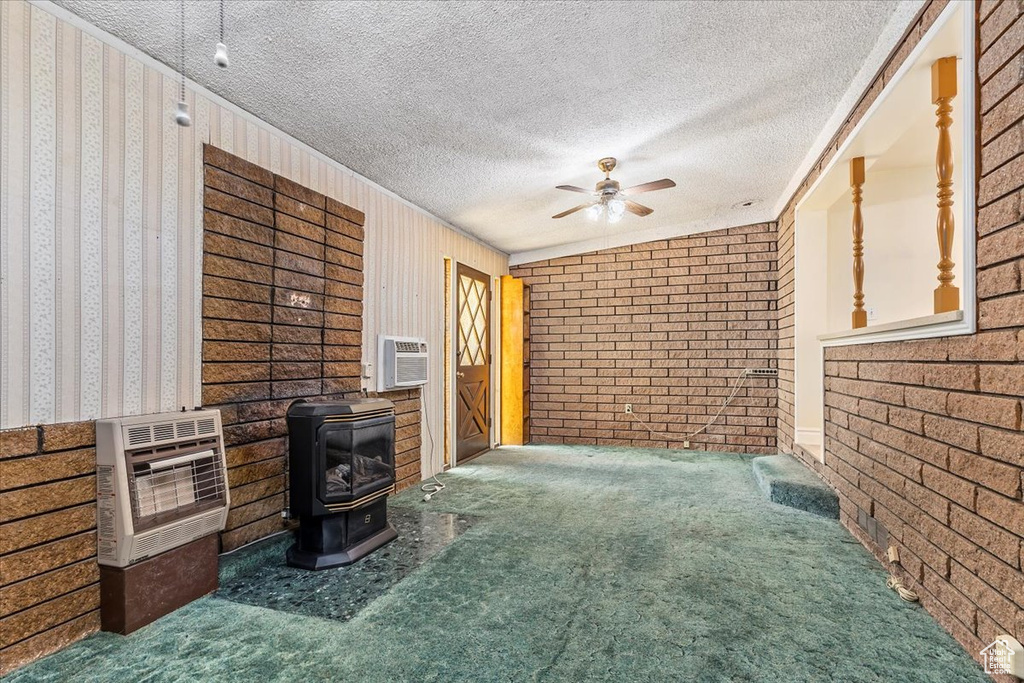 Unfurnished living room with heating unit, carpet flooring, a wood stove, a ceiling fan, and a textured ceiling