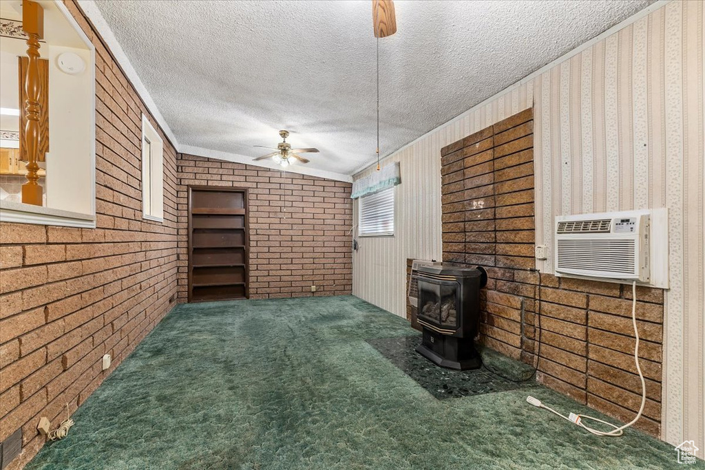 Unfurnished living room with a ceiling fan, a wood stove, ornamental molding, a textured ceiling, and carpet