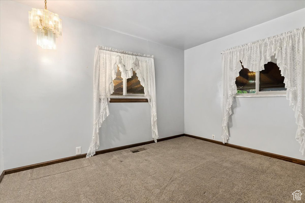 Carpeted spare room featuring a chandelier and baseboards