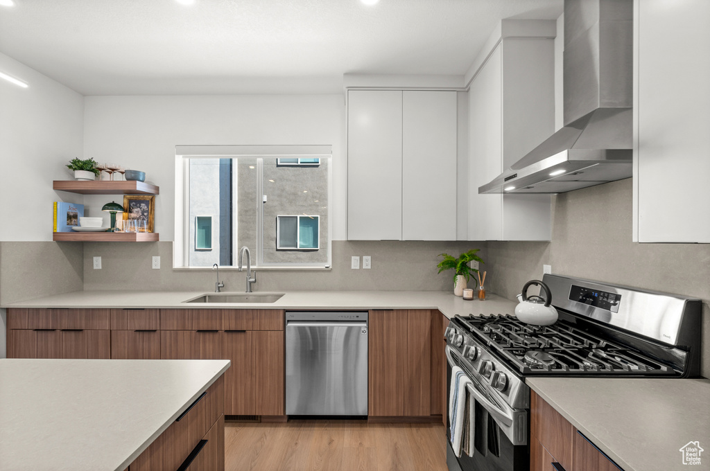 Kitchen featuring appliances with stainless steel finishes, wall chimney exhaust hood, modern cabinets, and light countertops