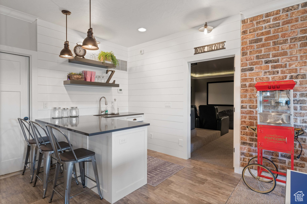 Kitchen with dark countertops, wood finished floors, a kitchen breakfast bar, and pendant lighting