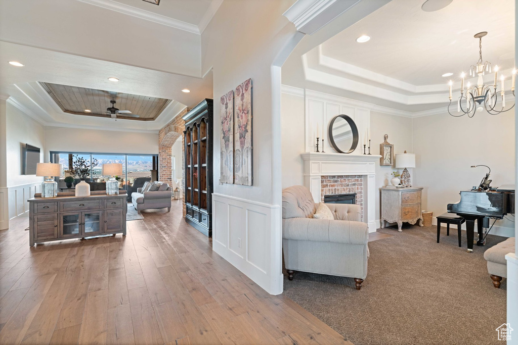 Living area featuring a tray ceiling, ornamental molding, wood-type flooring, a fireplace, and a chandelier