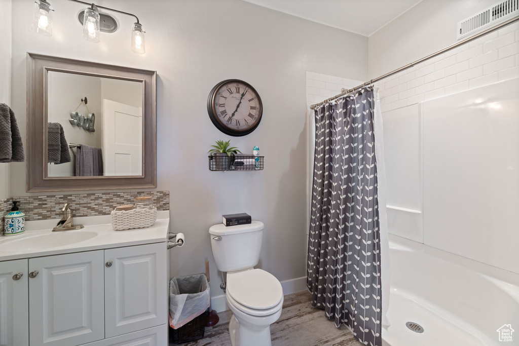 Full bath with a shower with curtain, vanity, wood finished floors, and decorative backsplash