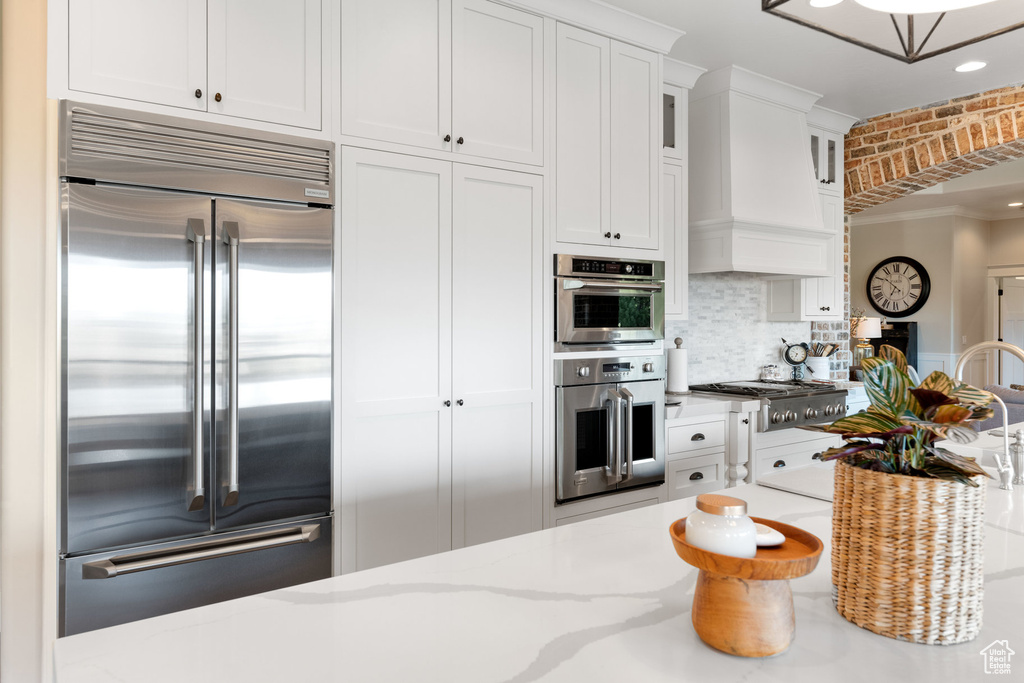 Kitchen featuring appliances with stainless steel finishes, white cabinets, decorative backsplash, glass insert cabinets, and light stone countertops
