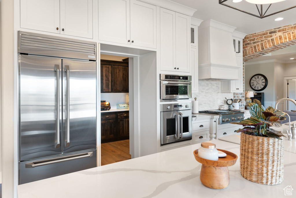Kitchen with stainless steel appliances, white cabinets, light stone counters, glass insert cabinets, and tasteful backsplash