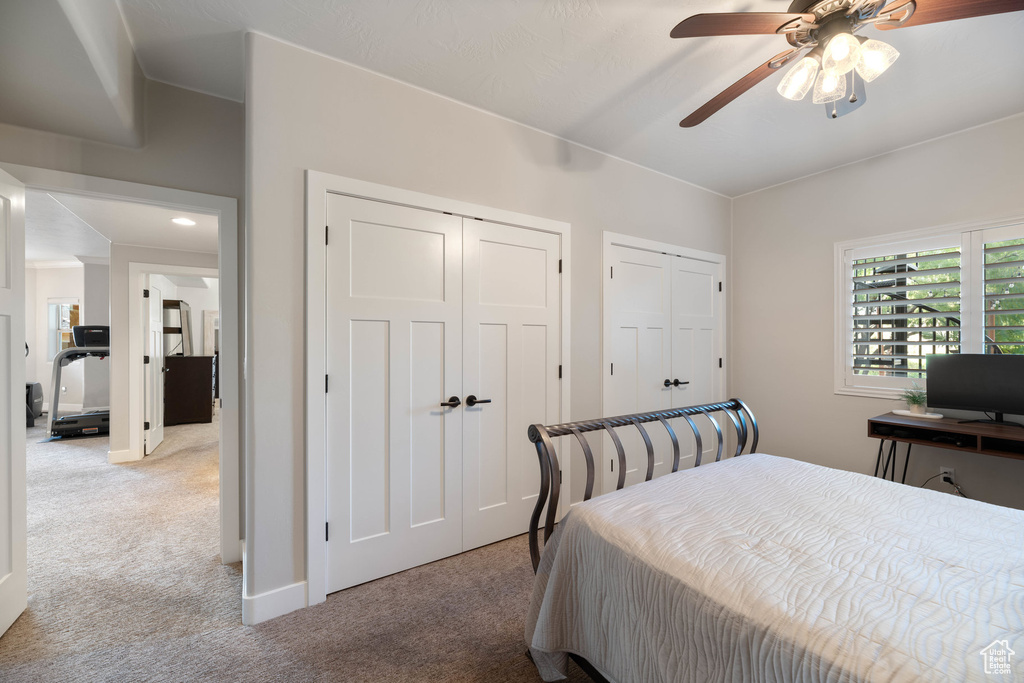 Bedroom featuring light carpet, two closets, and a ceiling fan