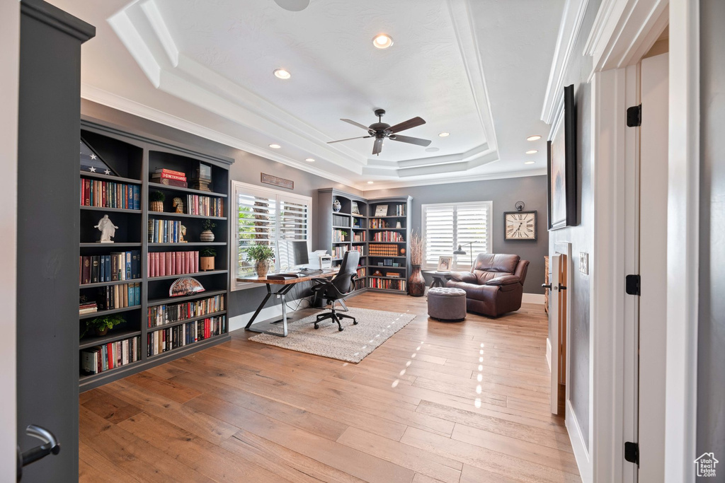 Office area with a raised ceiling, ceiling fan, crown molding, light wood finished floors, and recessed lighting