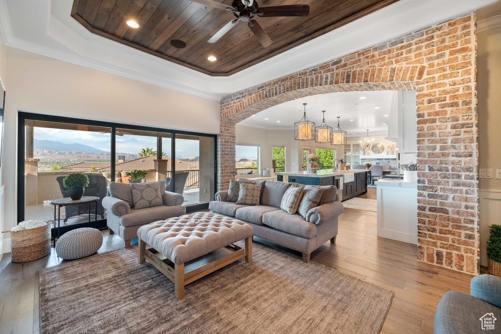 Living area featuring light wood-style floors, a tray ceiling, ceiling fan, crown molding, and wood ceiling