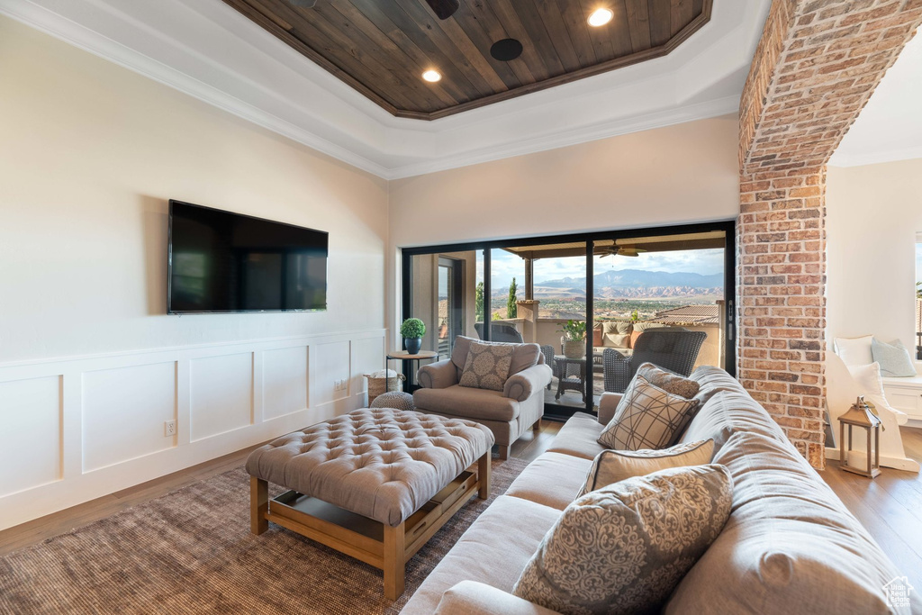 Living room with wood finished floors, a raised ceiling, ornamental molding, a decorative wall, and wainscoting