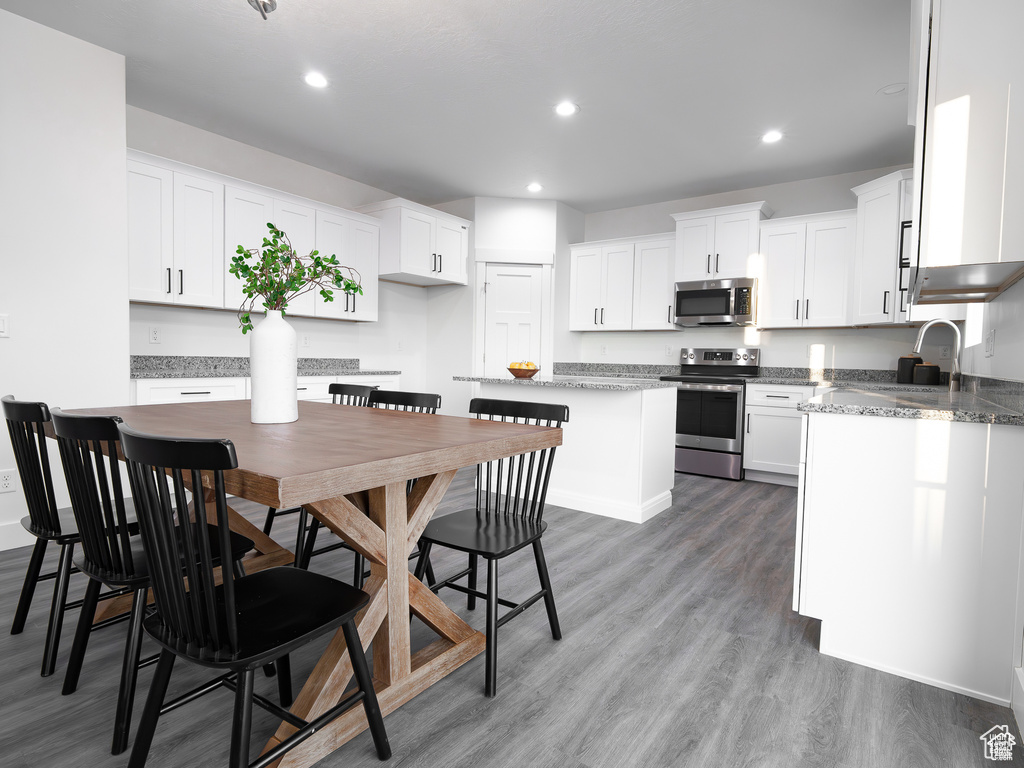 Kitchen featuring appliances with stainless steel finishes, wood finished floors, recessed lighting, white cabinets, and a center island