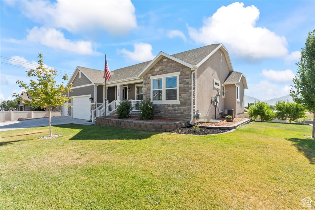 Single story home featuring stone siding, a garage, concrete driveway, a front lawn, and a porch