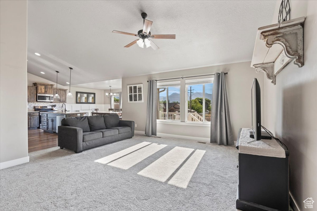 Living room with a ceiling fan, light colored carpet, vaulted ceiling, recessed lighting, and a chandelier