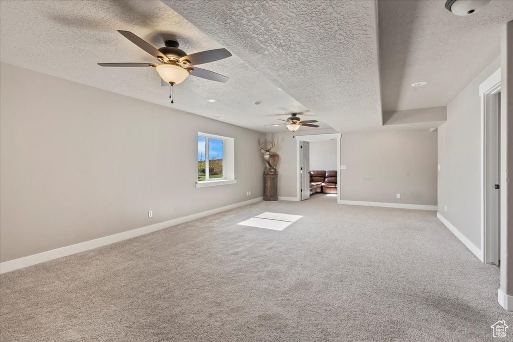 Unfurnished living room featuring a textured ceiling, a ceiling fan, and light carpet