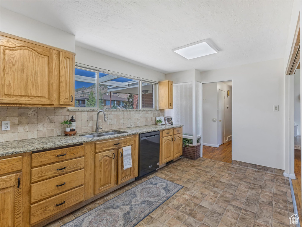 Kitchen featuring black dishwasher, decorative backsplash, light stone counters, and stone finish floors