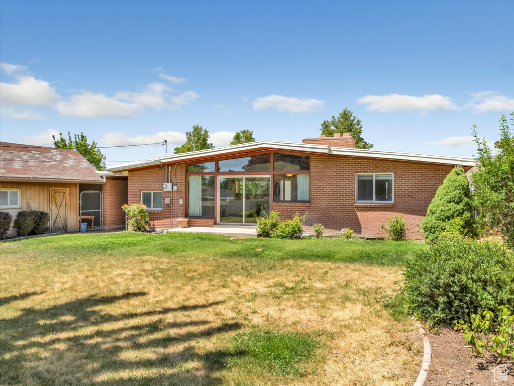 Back of property with brick siding, a lawn, and a chimney