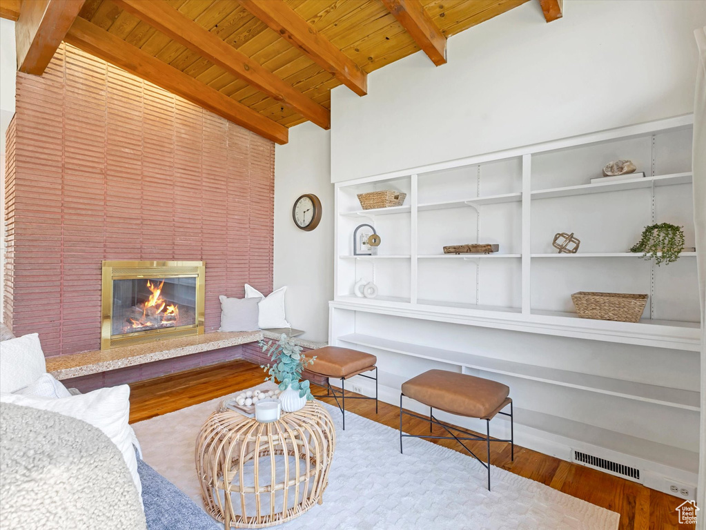 Living area featuring a wood ceiling with exposed beams, wood finished floors, a glass covered fireplace, and built in features