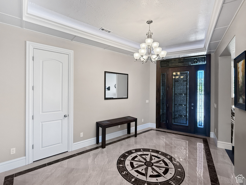 Foyer with inlaid floor details, a chandelier, marble tiled flooring, a raised ceiling, and crown molding