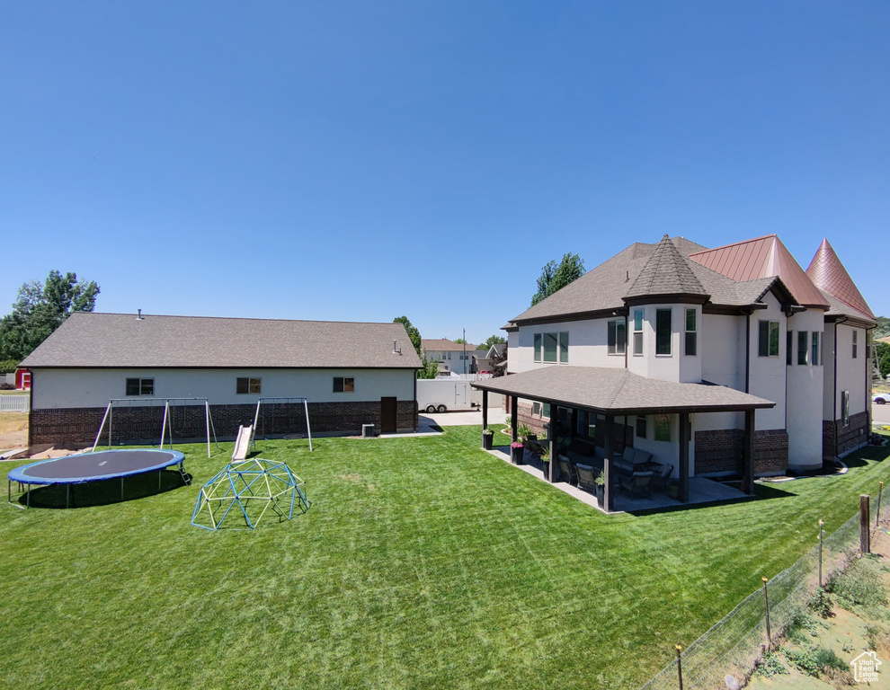 Rear view of house featuring a trampoline, a patio area, a fenced backyard, and stucco siding